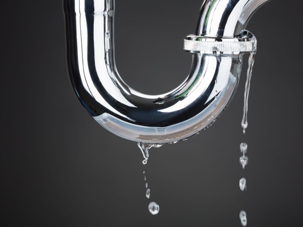 Chrome P-trap pipe with water drips falling from a worn slip-nut joint