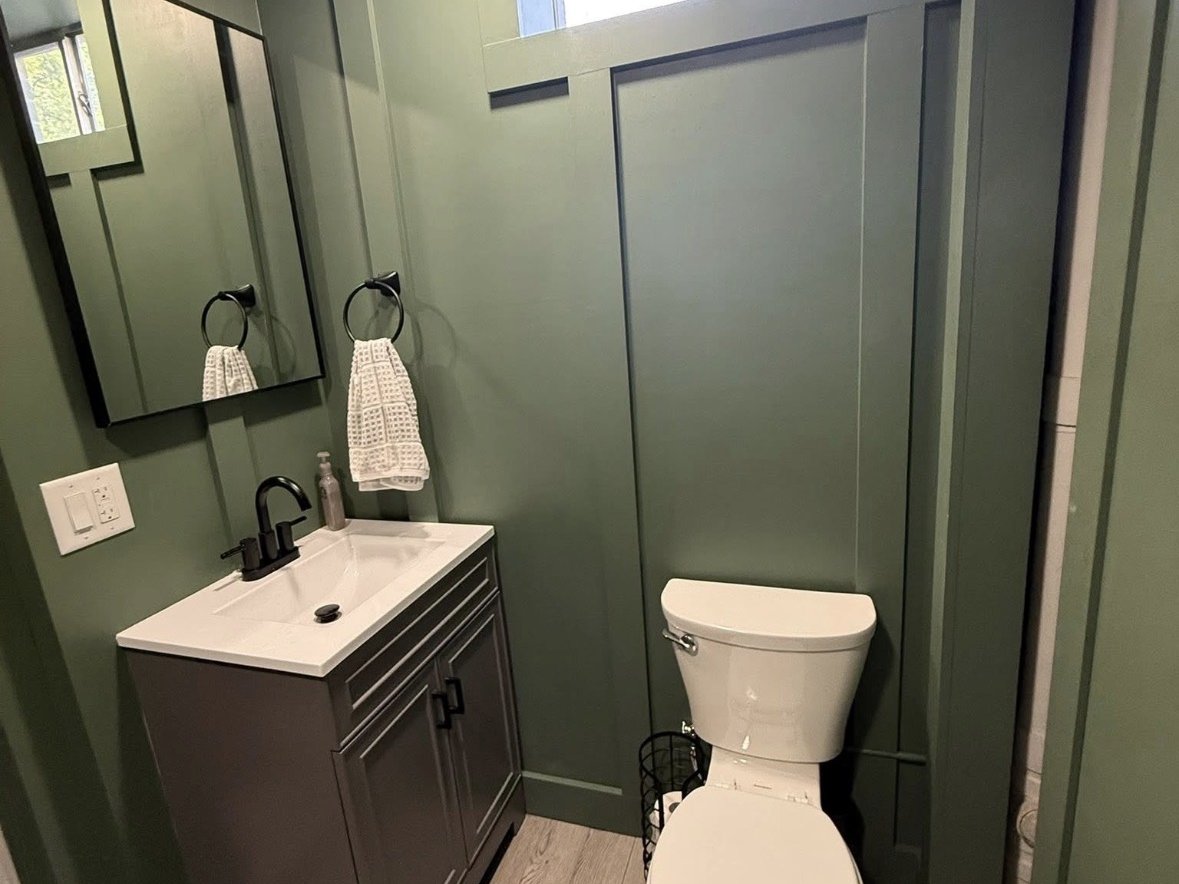 Remodeled bathroom with green walls, dark vanity with white countertop, framed mirror, and a modern toilet